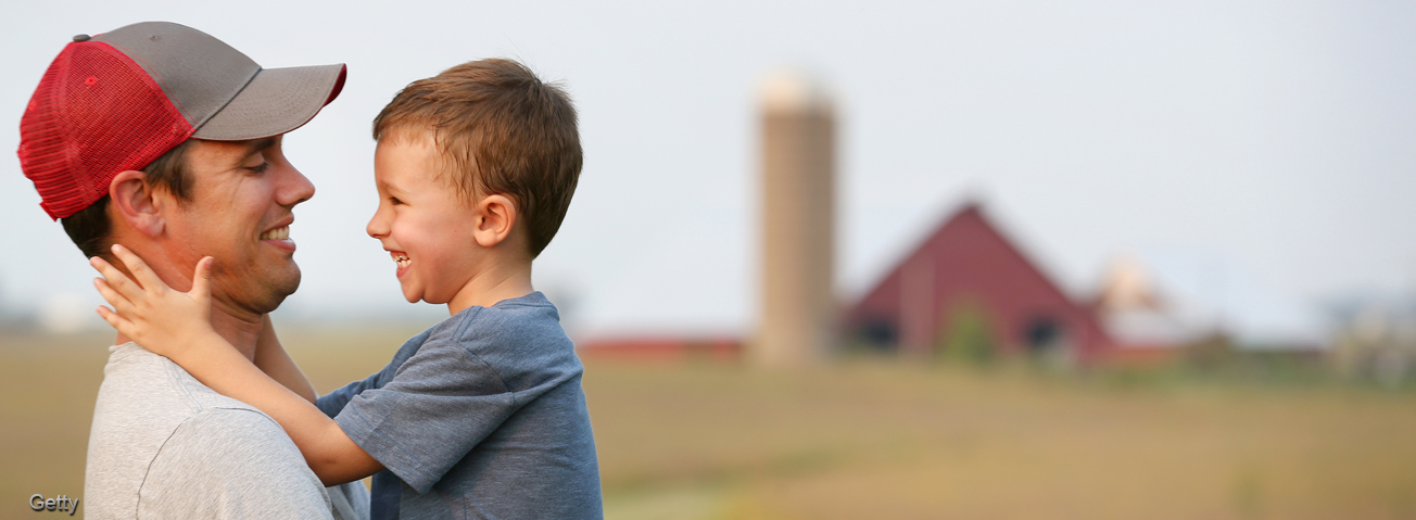 Farmer holding young son with farm and crop in background