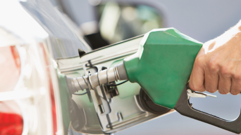 Photo of a hand holding a gas pump and filling a car with gas.